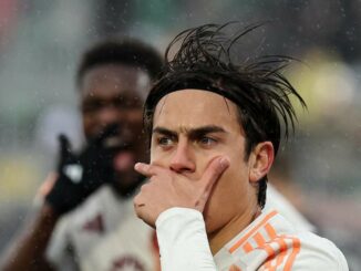 Footballeur célébrant sous la pluie, main sur le visage.