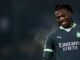 Footballeur souriant en maillot sombre, fond flou.