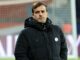 Homme en manteau noir devant but de football.