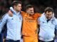 Deux hommes soutenant un joueur de football blessé.