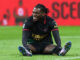 Joueur de football assis sur le terrain, souriant.