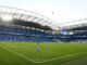 Stade de football vide avec tribunes bleues.