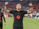 Joueur de football levant les bras sur le terrain.