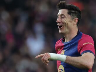 Joueur de football souriant en maillot rouge et bleu.