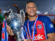 Joueur de football tenant un trophée argenté au stade.