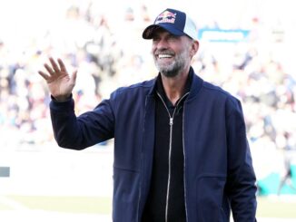 Homme souriant avec casquette, saluant foule.