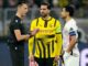 Arbitre discutant avec joueurs de football sur le terrain.