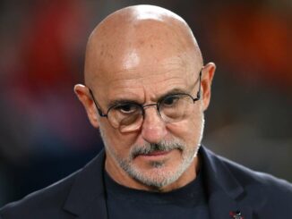 Homme chauve avec lunettes et barbe regardant vers le bas.