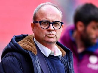 Homme avec lunettes et manteau, arrière-plan flou.