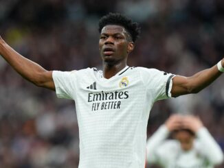 Footballeur en maillot blanc bras écartés sur terrain.