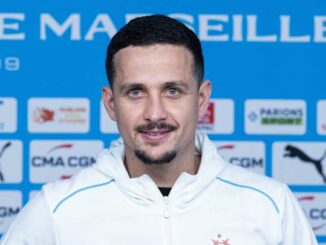 Personne devant panneau OM et sponsors sportifs.