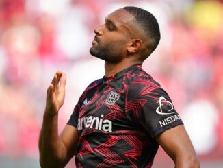 Footballeur en maillot rouge et noir sur terrain.