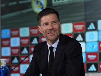 Homme souriant en costume lors d'une conférence de presse.