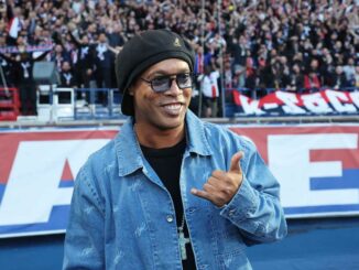 Homme souriant portant une veste en jean devant foule.