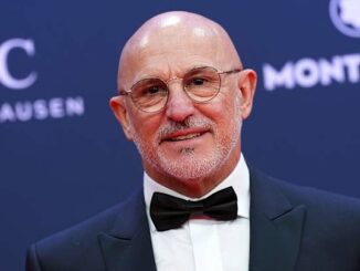 Homme en smoking avec lunettes sur tapis rouge.