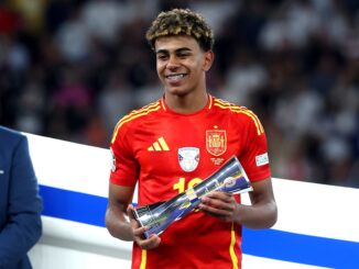Joueur de football en maillot rouge avec un trophée.