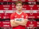 Jeune joueur de football en maillot rouge devant logo.