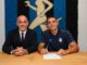 Deux hommes souriants signent un document.