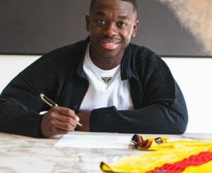 Homme souriant signant un document à une table.