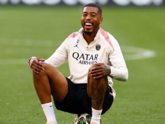 Joueur de football souriant assis sur terrain.