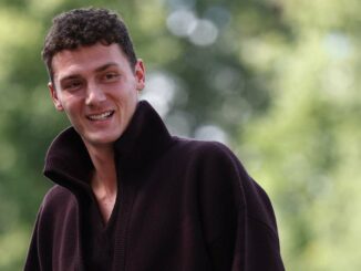 Homme souriant portant un pull foncé, fond flou.
