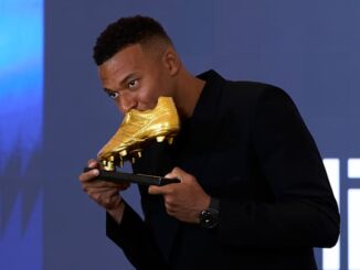 Homme posant avec un trophée de chaussure en or.