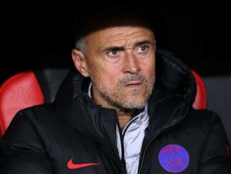 Homme en veste PSG dans un stade sombre.