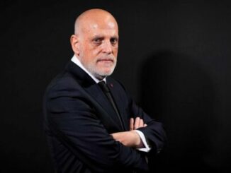 Homme en costume sombre, bras croisés, fond noir