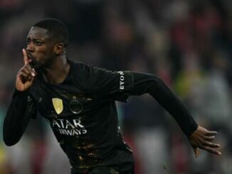 Footballeur en noir célébrant avec geste silence