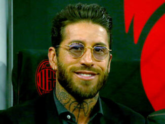 Homme souriant en costume devant logo rouge