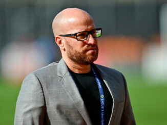 Homme chauve en blazer gris au stade