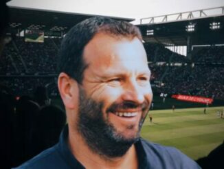 Homme souriant devant un stade de football